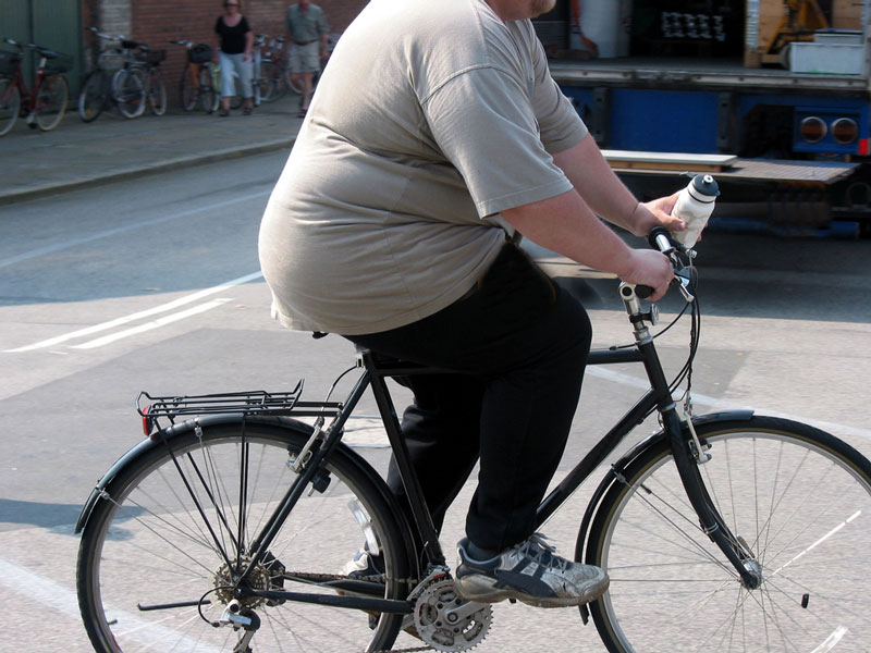 Übergewichtige Frau auf dem Fahrrad: wir beeinflussen durch unser Verhalten unser Dicksein