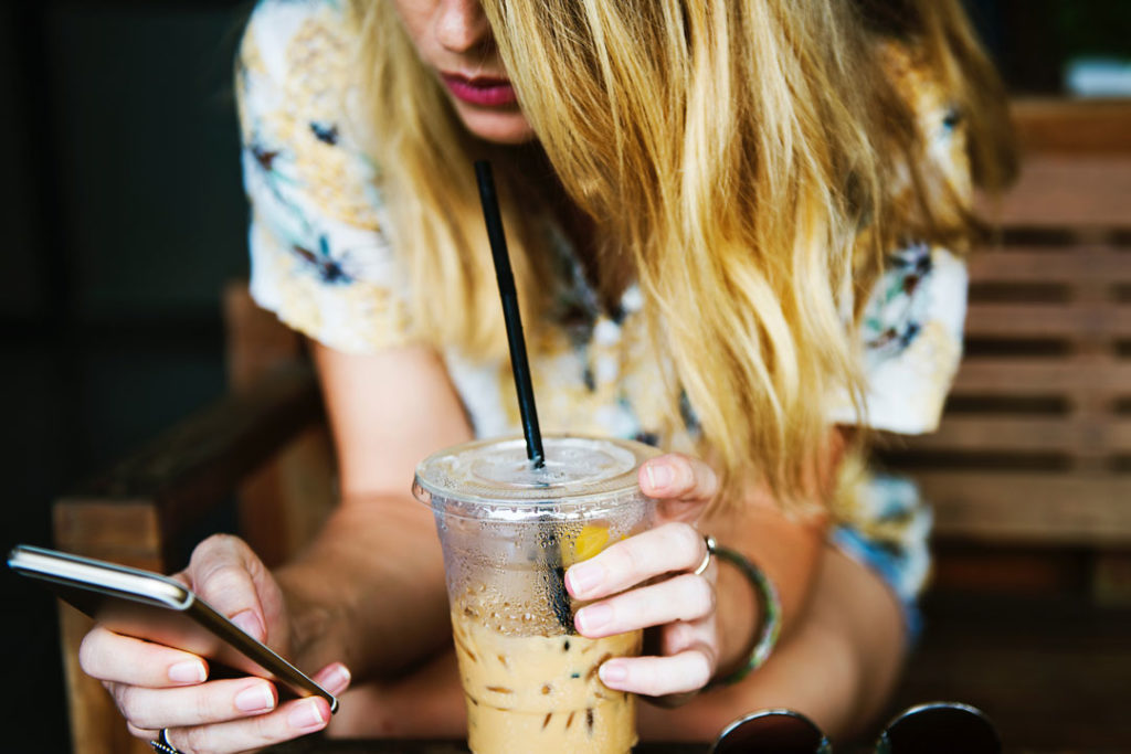 Eiskaffee trinken mit Smartphone in der Hand. Berufs- und Privatleben kann Stress verursachen