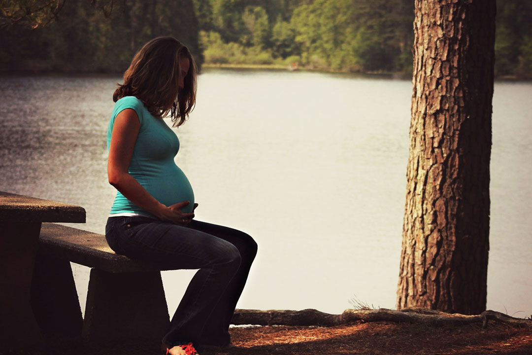 Schwangere Frau sitzt auf Steinbank am See