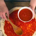 Eine Pizza wird mit Tomatensauce belegt