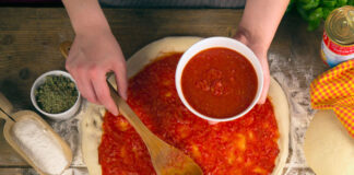 Eine Pizza wird mit Tomatensauce belegt