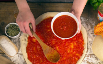 Eine Pizza wird mit Tomatensauce belegt