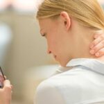 Eine junge Frau hat Nackenschmerzen aufgrund der häufigen Smartphone-Nutzung