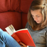 Eine Junge Frau liest rückenfreundlich ein Buch auf der Couch
