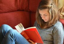 Eine Junge Frau liest rückenfreundlich ein Buch auf der Couch
