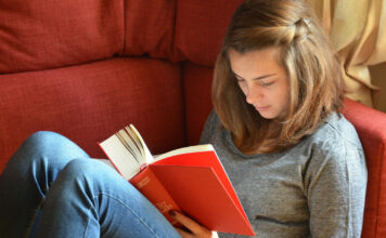 Eine Junge Frau liest rückenfreundlich ein Buch auf der Couch