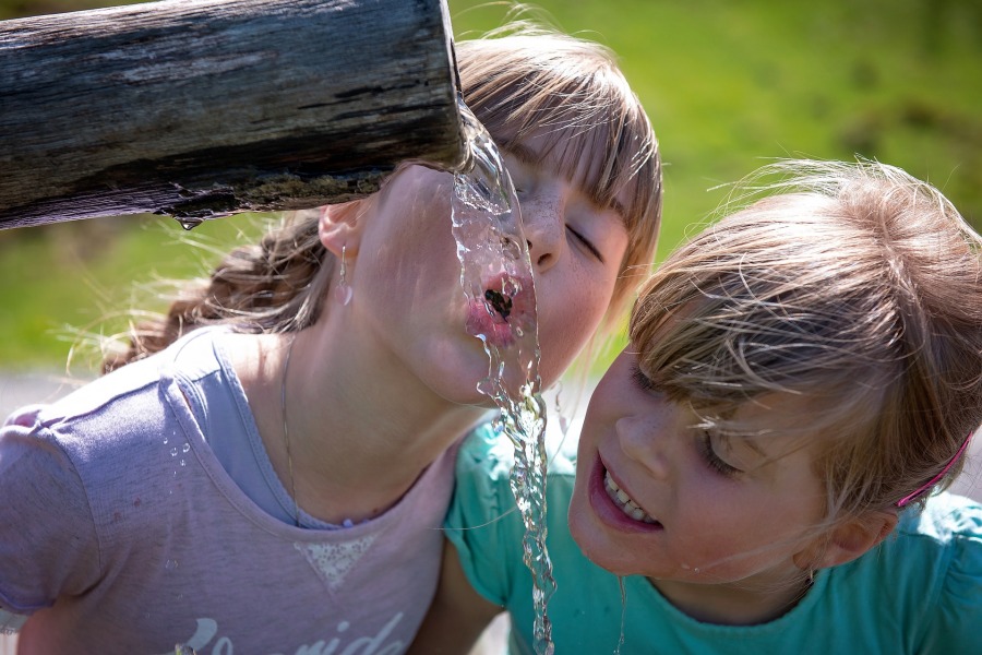 Zwei Kinder trinken Wasser aus einer Quelle