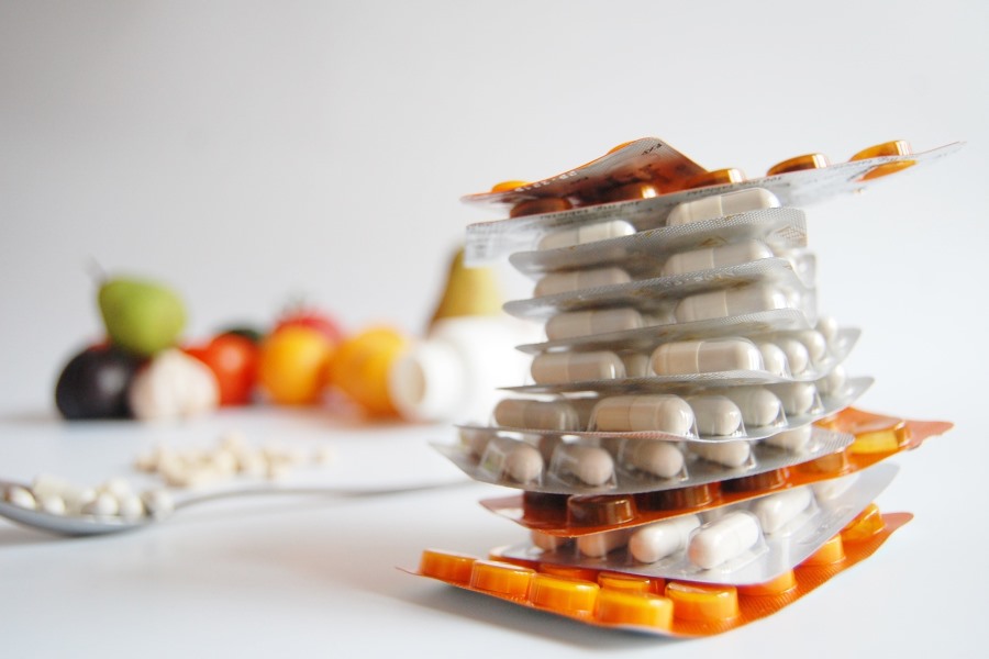 Ein Stapel Tabletten im Vordergrund, im Hintergrund Obst und Gemüse